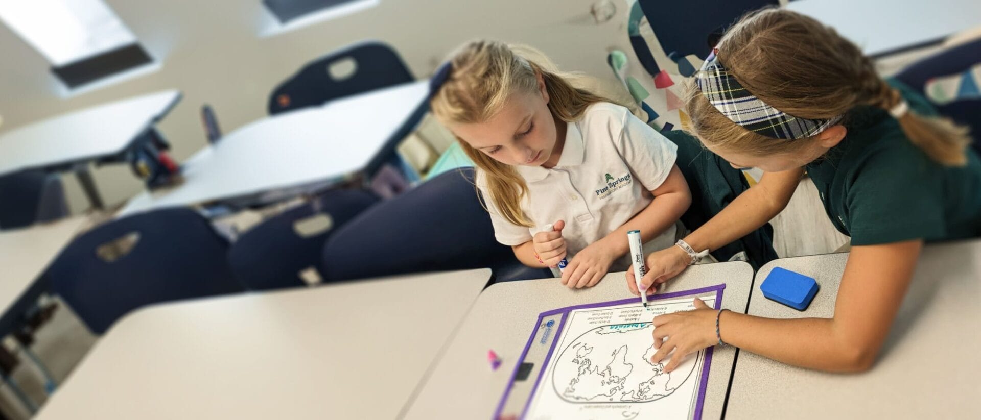 Two young girls working together on an assignment in a classroom.