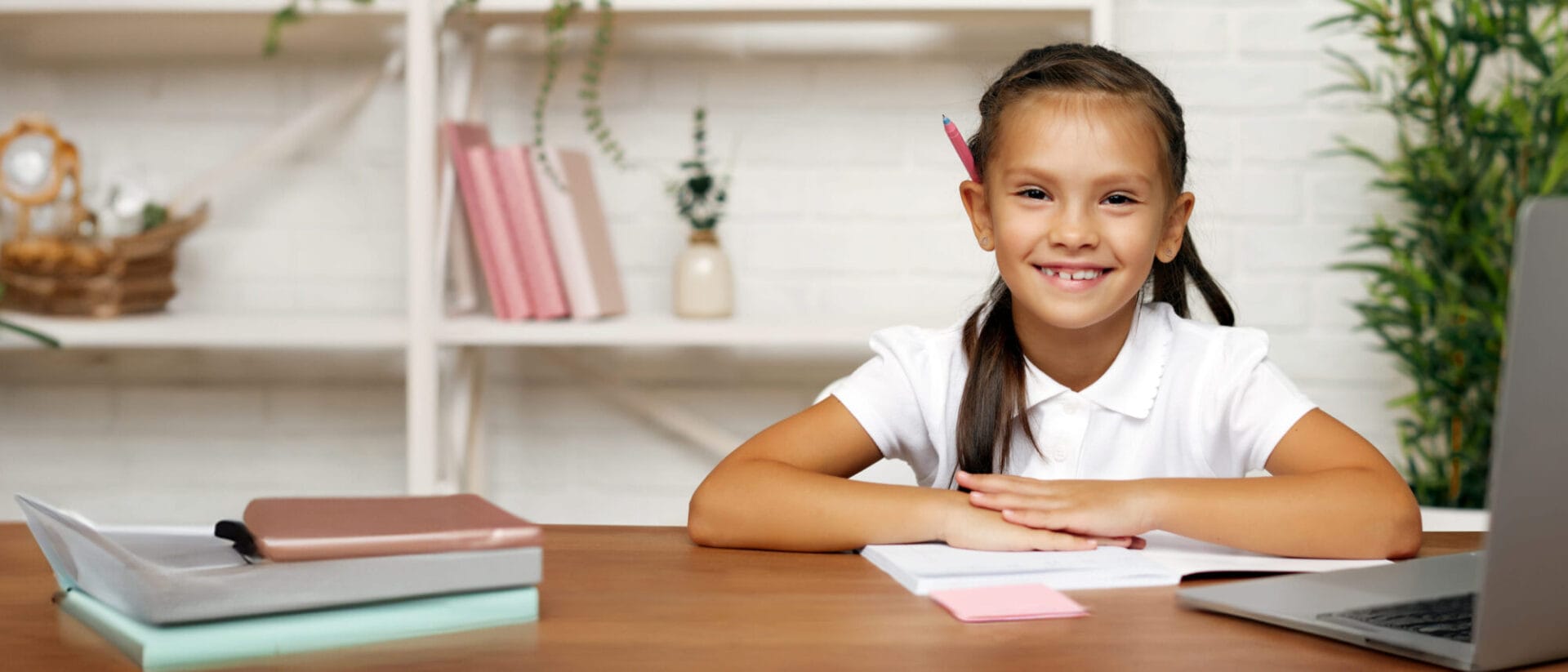 A young girl happily smiles while sitting at a desk with a laptop.